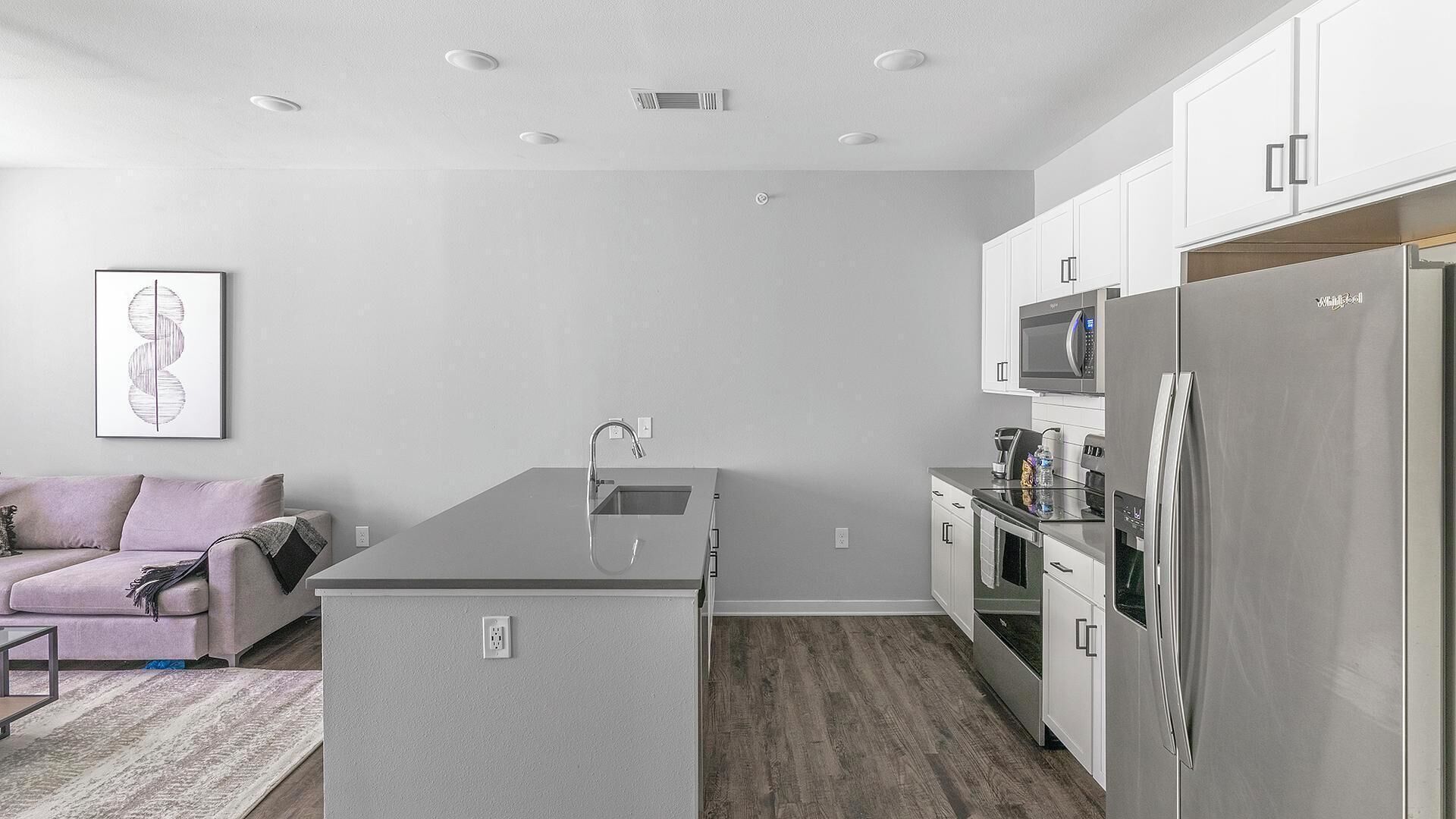 A modern kitchen with white cabinets, a stainless steel refrigerator, and a built-in microwave.
