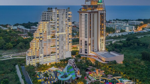 Un hotel de gran altura con varios pisos, una piscina en la azotea y un parque acuático con toboganes y juegos.