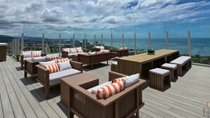Una terraza en la azotea con mobiliario de mimbre, una cubierta de madera y una vista panorámica de la ciudad y el océano.