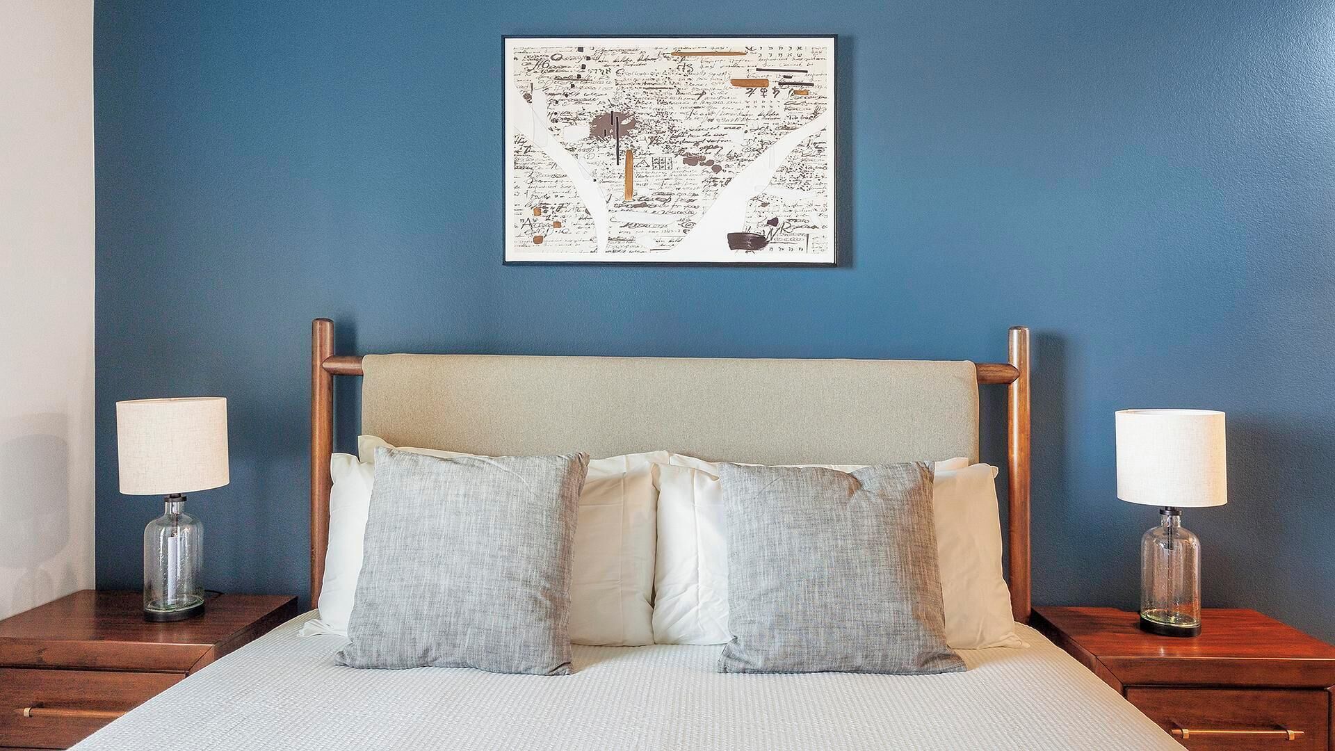 A neatly made bed with a headboard, two bedside lamps, and a framed artwork on the wall.