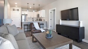 A modern living room with a sofa, coffee table, and a TV mounted on the wall. - Landing | Beautiful 2BD, Clubhouse (Goodyear)