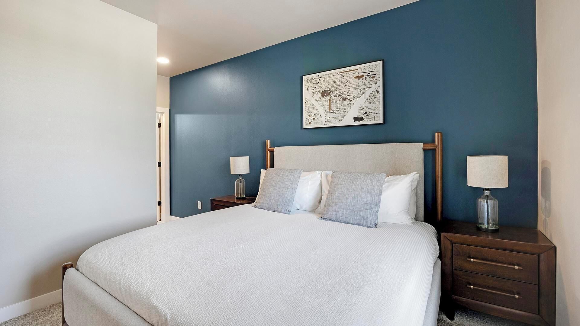 A bedroom with a large bed, two bedside tables, and a wall-mounted artwork.