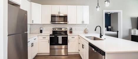 A modern kitchen with stainless steel appliances, white cabinetry, and a wooden floor.