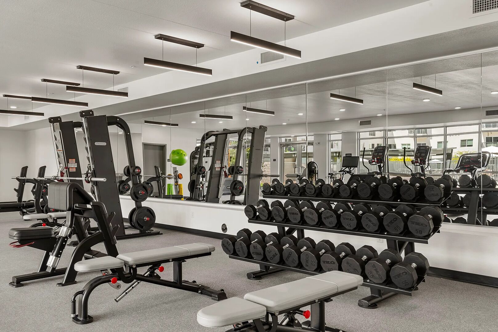A modern gym with weightlifting equipment, benches, and a mirrored wall.