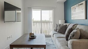 A modern living room with a grey sofa, a wooden coffee table, and a balcony with a view. - Landing | Stylish 1BD, Gym, Pool (Phoenix)
