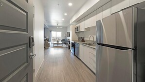 A modern kitchen with stainless steel appliances, a central island, and a view into the living area. - Landing | Chic 1BD, Gym, Pool (Phoenix)