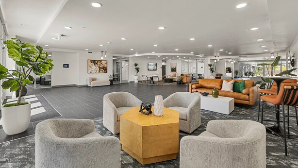 A spacious lobby with grey upholstered chairs, a wooden coffee table, and a reception area with a sofa and a TV. - Landing | Chic 1BD, Gym, Pool (Phoenix)