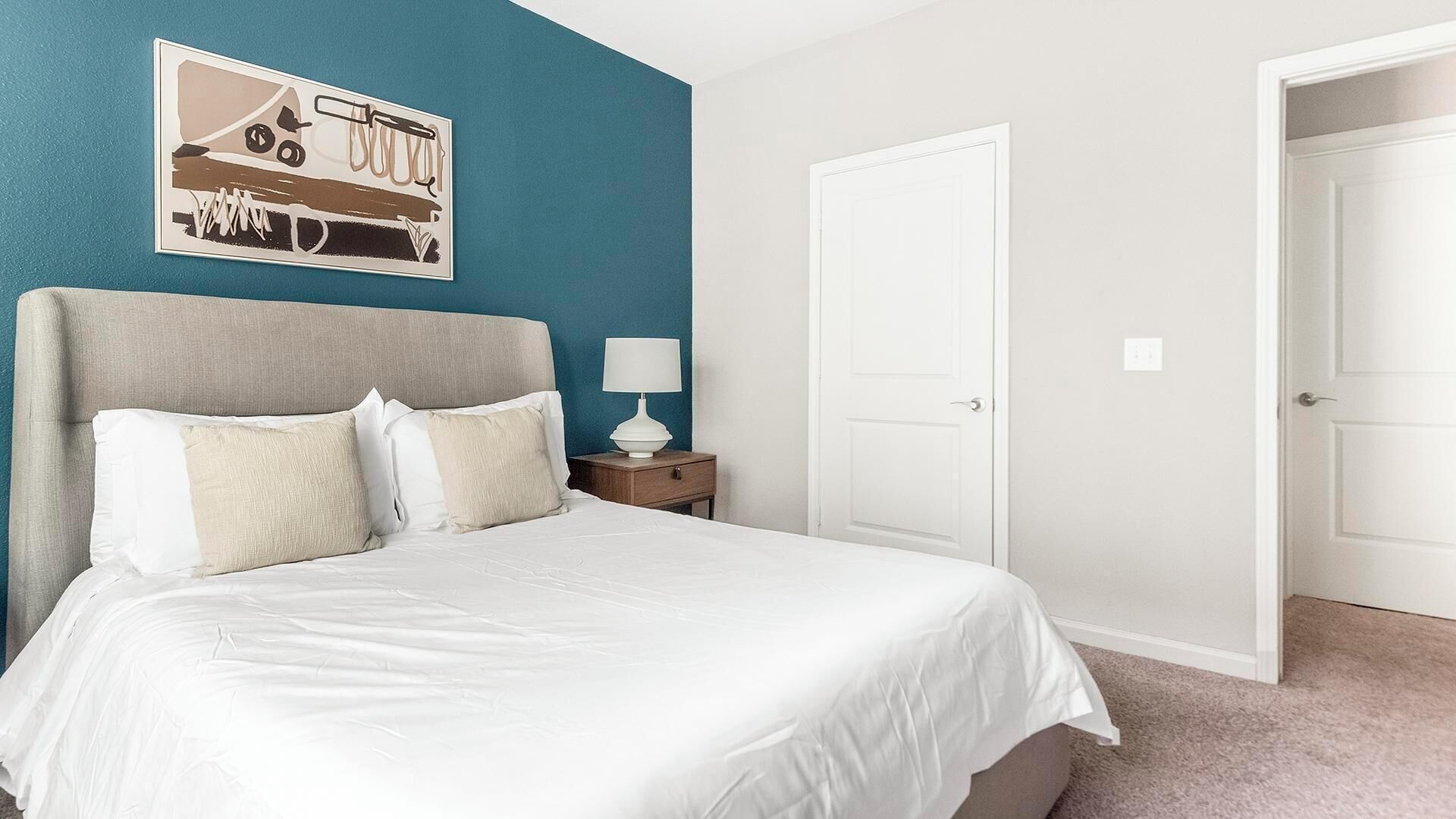 A bedroom with a bed, a nightstand, a lamp, and a door.
