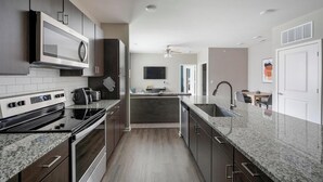 Une cuisine moderne dotée d’un four, d’un micro-ondes et d’une plaque de cuisson intégrés. Elle se caractérise par des meubles de cuisine en bois foncé, un plan de travail en granit et un petit îlot central avec un évier.