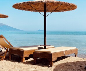 Ein Strand mit Holzliegen und einem Strohdachschirm.