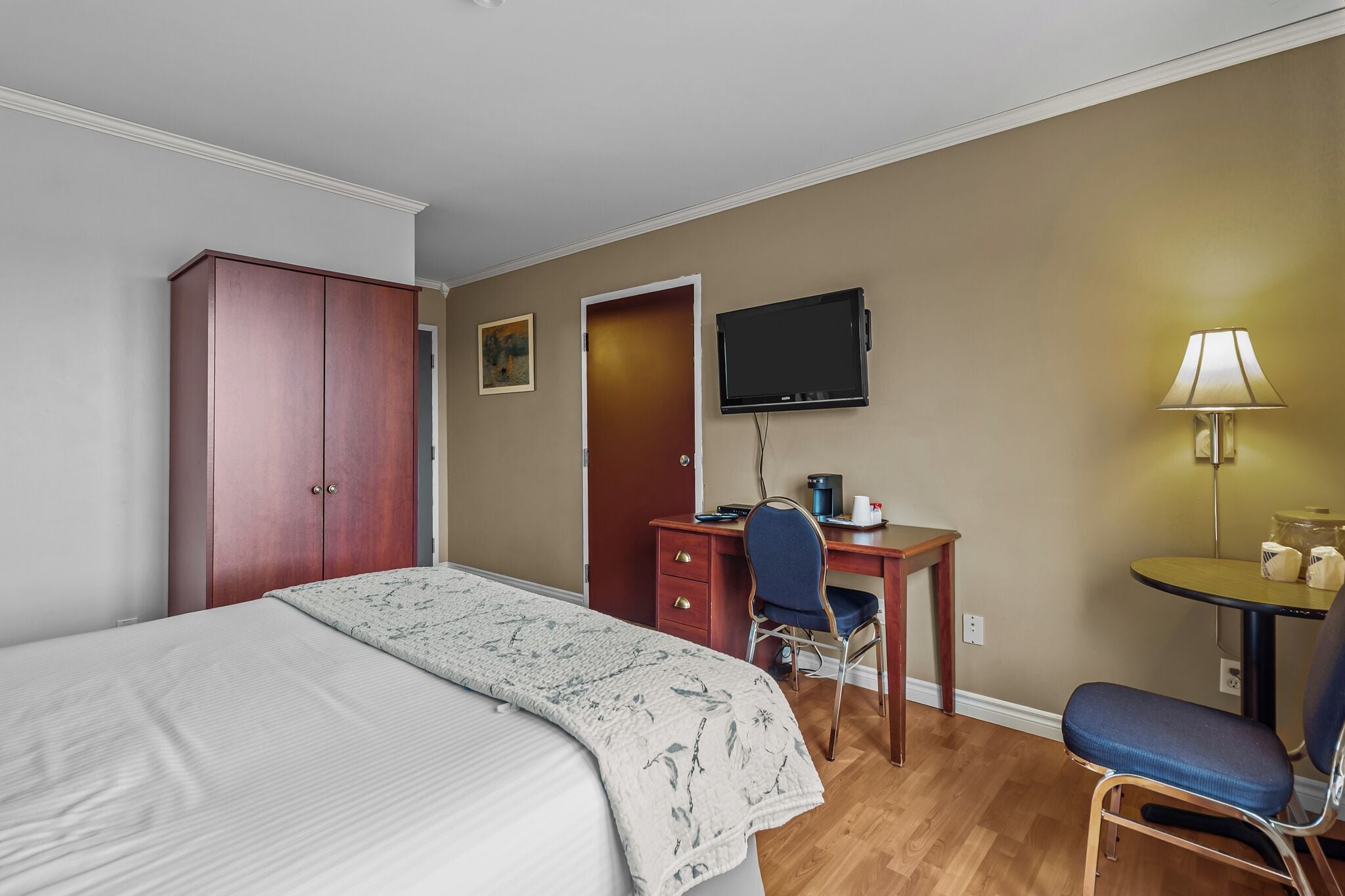 A hotel room with a bed, a desk with a chair, a television, and a lamp.