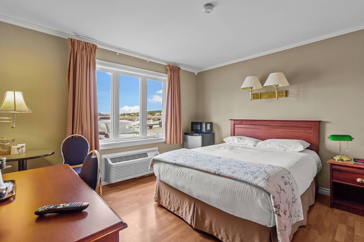 A hotel room with a bed, a desk, a chair, a TV, a lamp, and a window with curtains.