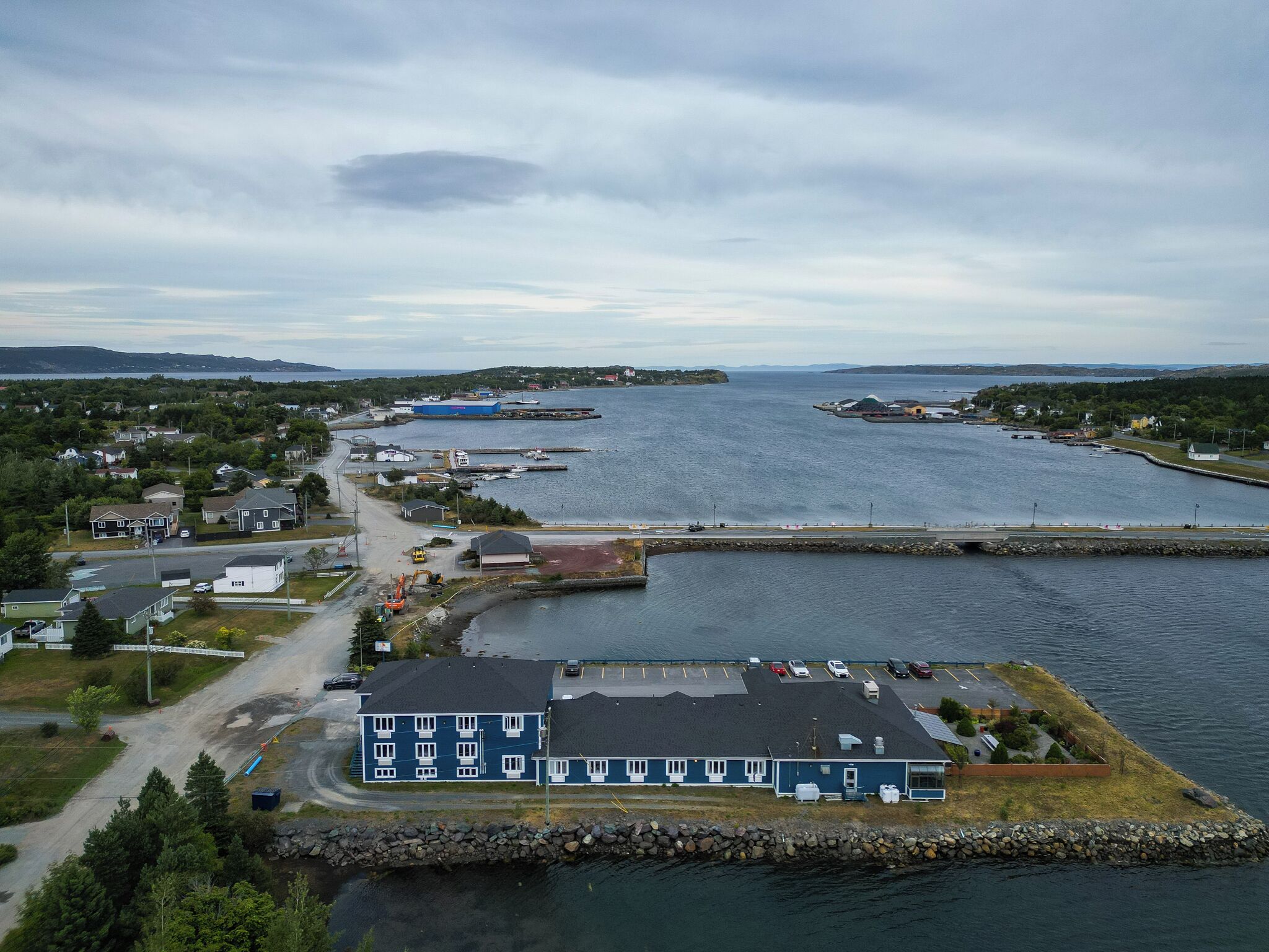 An aerial view of a coastal town with a marina, a large blue building, and a small island with a parking lot.