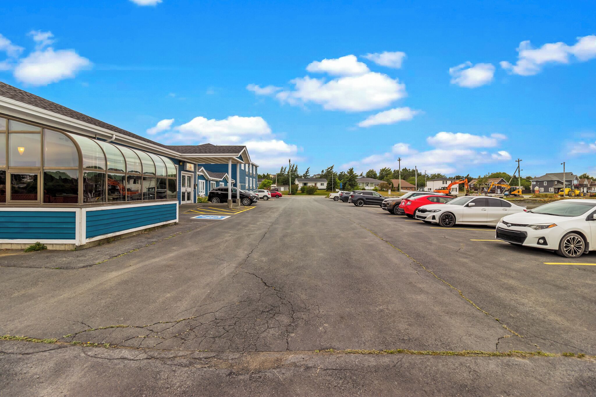A parking lot with several cars and a building with a blue exterior and large windows.
