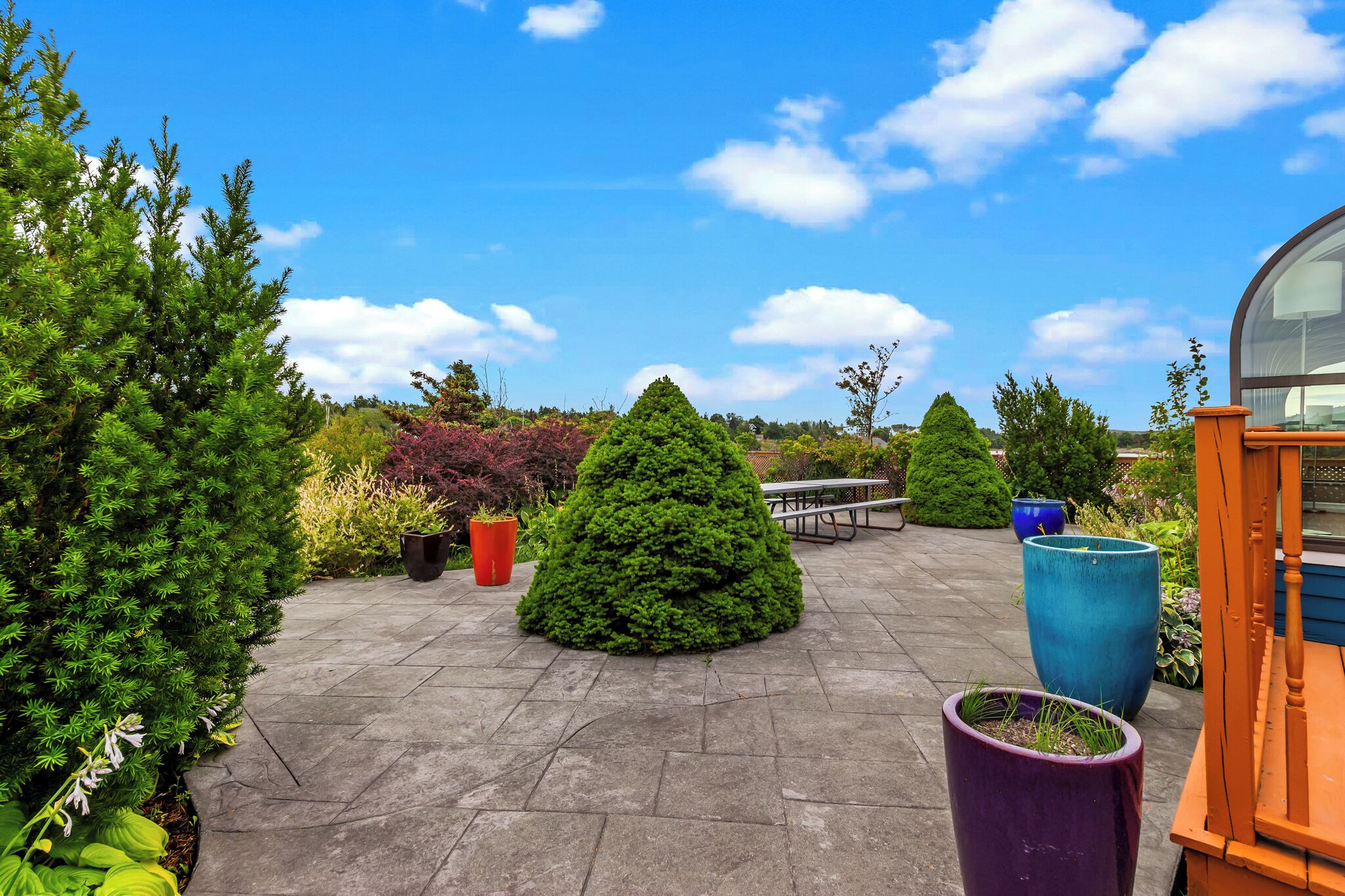 A patio area with a stone floor, large potted plants, a picnic table, and a wooden bench.