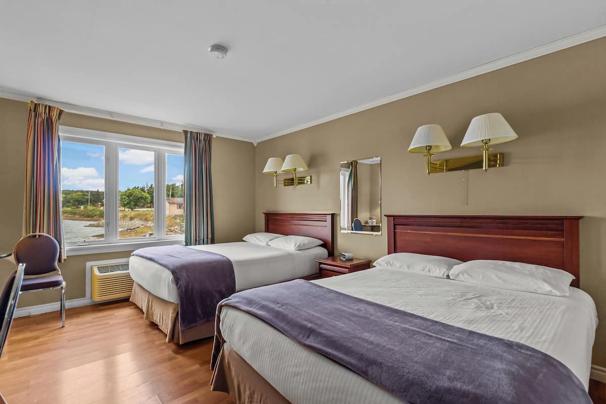 A hotel room with two beds, a chair, a desk, and a window with curtains.