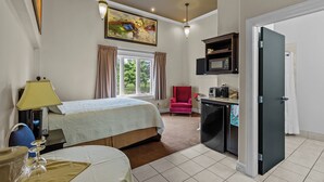 A hotel room with a bed, a desk with a microwave, a red chair, and a painting on the wall. - Bayview Inn (Bay Roberts)