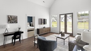 Un salon moderne doté d’une grande fenêtre, d’un téléviseur à écran plat, d’un bureau et d’un coin salon confortable.
