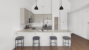 Une cuisine moderne avec des meubles blancs, des appareils en acier inoxydable et un îlot central doté de tabourets de bar.