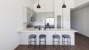 A modern kitchen with white cabinetry, stainless steel appliances, and a central island with bar stools. - Landing | Amazing 2BD, Clubhouse, Gym (Athens)