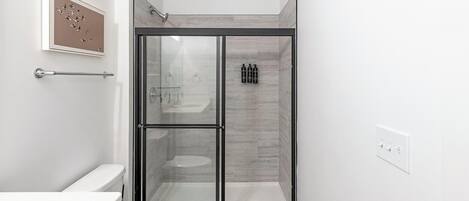 A modern bathroom with a glass-enclosed shower, a toilet, and a framed artwork on the wall.