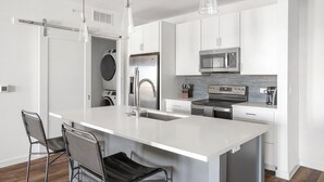 A modern kitchen with white cabinetry, stainless steel appliances, and a central island with bar stools.
