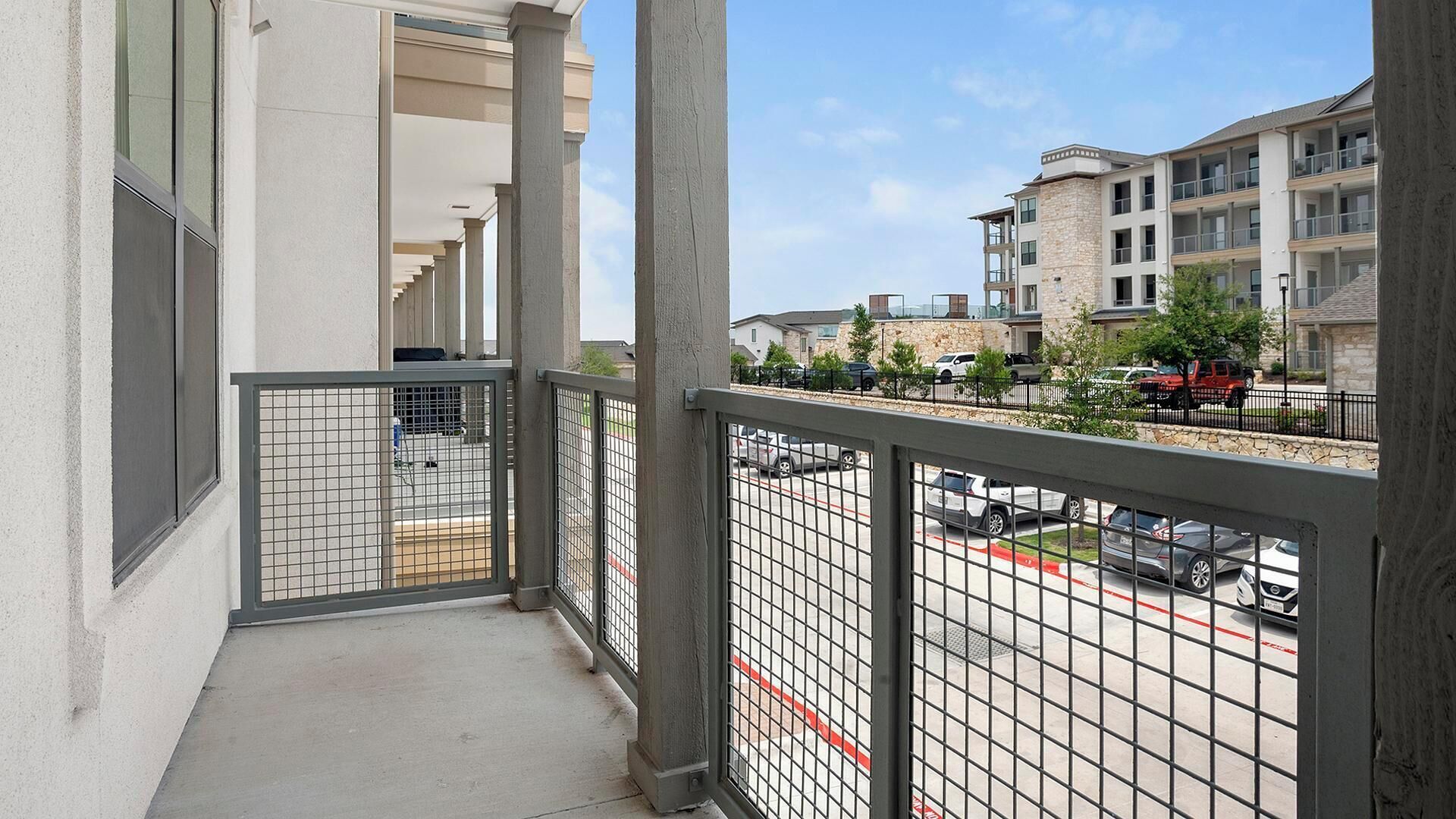 A balcony with a metal railing overlooking a parking area and residential buildings.