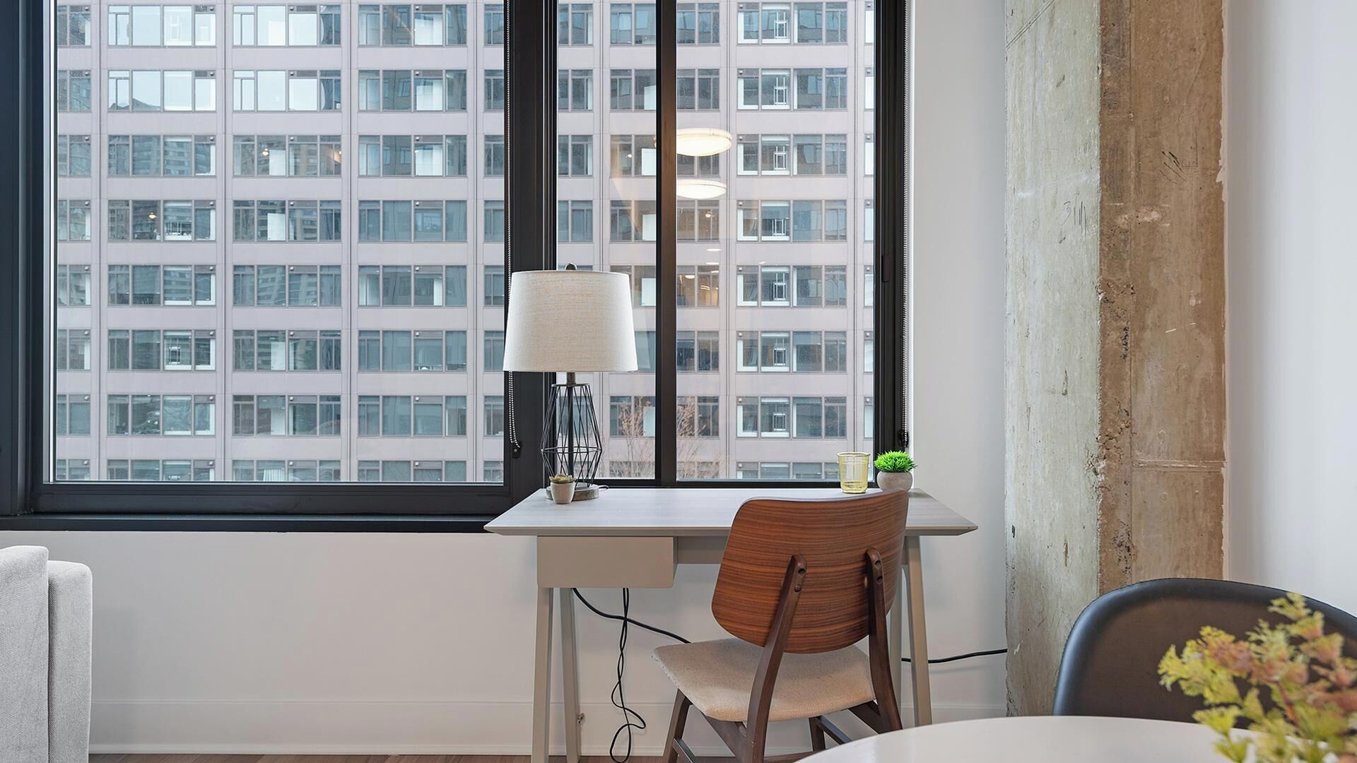 A modern office space with a desk, chair, and a large window offering a view of a high-rise building.