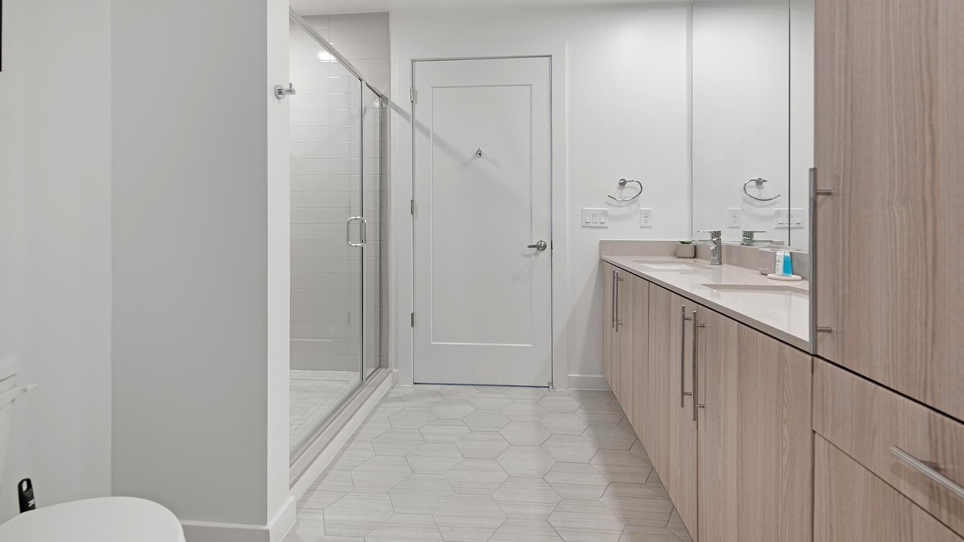 A modern bathroom with a glass shower, a white door, and a vanity with a mirror.