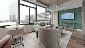 A modern living room with a sofa, armchairs, a coffee table, and a TV on a green wall.
