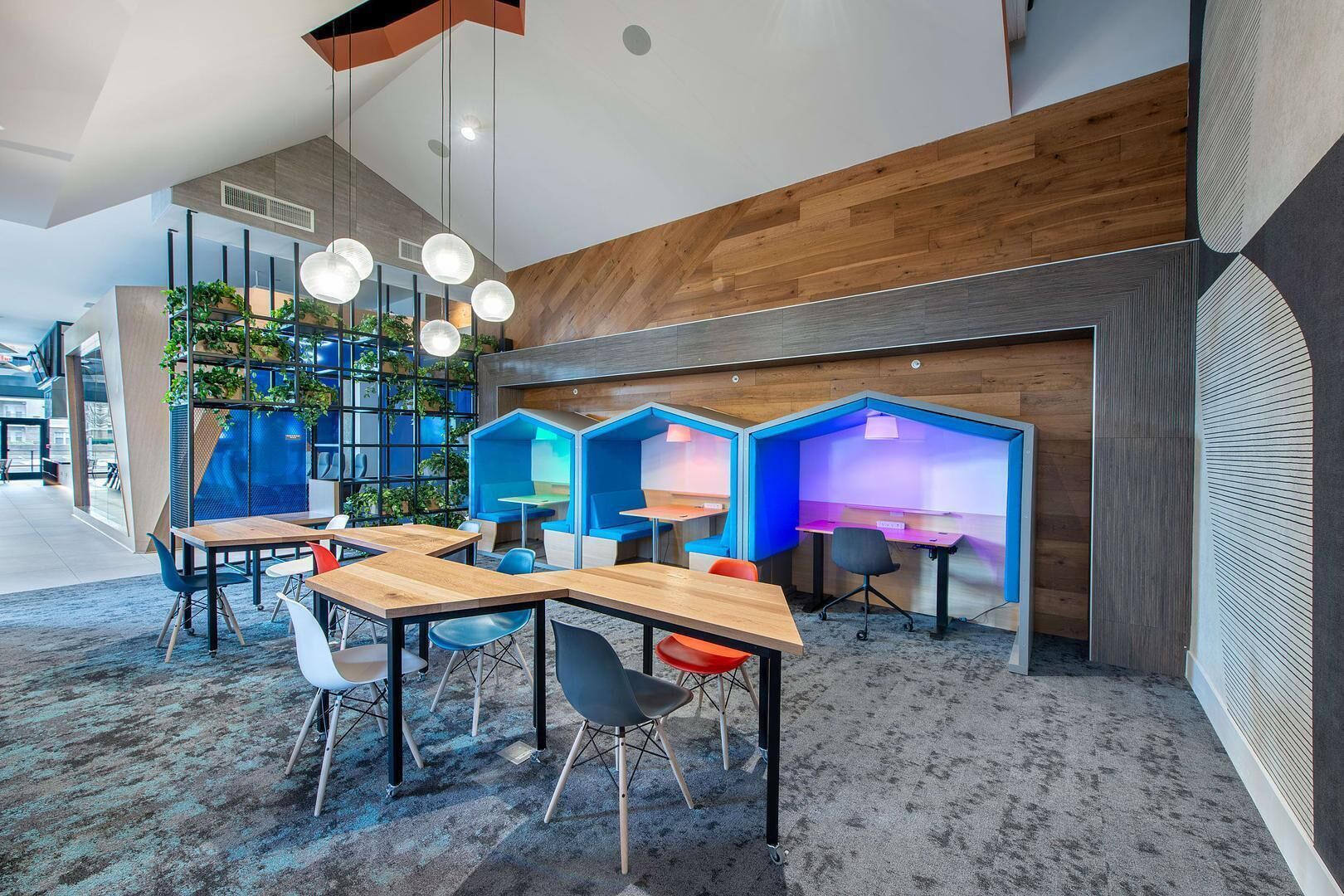 A modern office space with wooden desks, blue seating pods, and hanging pendant lights.