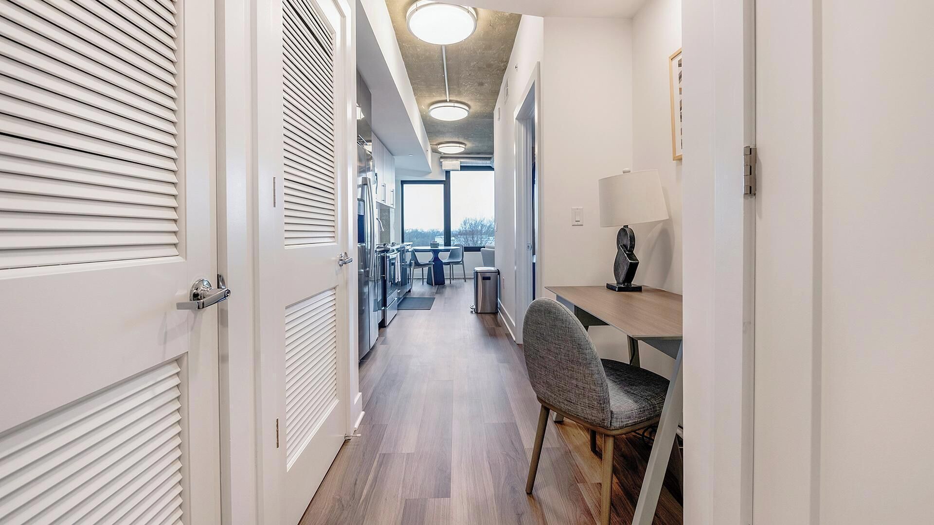 A modern hallway with a wooden floor, white doors, and a dining area with a table and chairs.