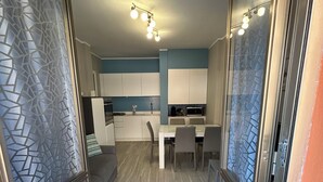 Et moderne køkken med hvide skabe, et spiseområde med bord og stole, og en gang med glasdøre med satin finish.