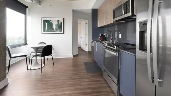 A modern kitchen with stainless steel appliances, a dining area with a table and chairs, and a cityscape artwork on the wall.