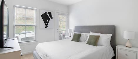 Un dormitorio con una cama grande, una mesita de noche con lámpara y un televisor sobre un mueble.