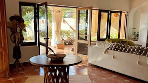 A room with a round wooden table, a sofa, and a view through large windows.