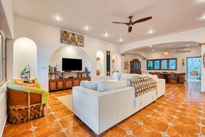 A spacious living room with a large sofa, a television, and a dining area with wooden furniture.