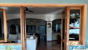 A spacious room with a large bed, a wooden door leading to another room, and a view of the sea through a window.