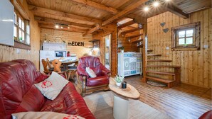 Un intérieur de chalet chaleureux avec un plafond en bois, un canapé en cuir rouge, un coin repas et une cuisine agrémentée d'une enseigne « MEDEN ».