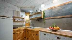 Une cuisine avec des meubles de rangement en bois, un réfrigérateur blanc, un évier et un panier de fruits posé sur le plan de travail.
