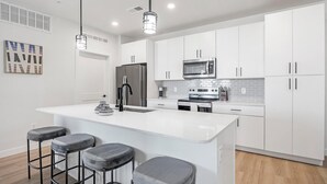 A modern kitchen with white cabinets, stainless steel appliances, and a central island with bar stools.