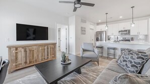 A modern living room with a flat-screen TV, wooden cabinet, grey sofa, and a coffee table.