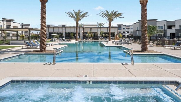 A pool area with multiple palm trees, lounge chairs, and a hot tub.