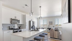 Una cocina moderna con armarios blancos, electrodomésticos de acero inoxidable y una isla central con taburetes.