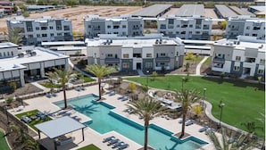 Un moderno complejo de apartamentos con piscina central, rodeado de palmeras y sillones de descanso.