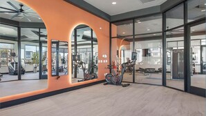 Un gimnasio amplio con equipamiento de ejercicio, ventanas grandes y un ventilador de techo moderno.