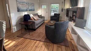 Un salón amplio con suelo de madera, un sofá gris, un sillón redondo de color gris y un televisor de pantalla plana montado en la pared.