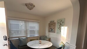 Una habitación acogedora con una mesa redonda, sillas azules, un banco y una ventana con persianas.