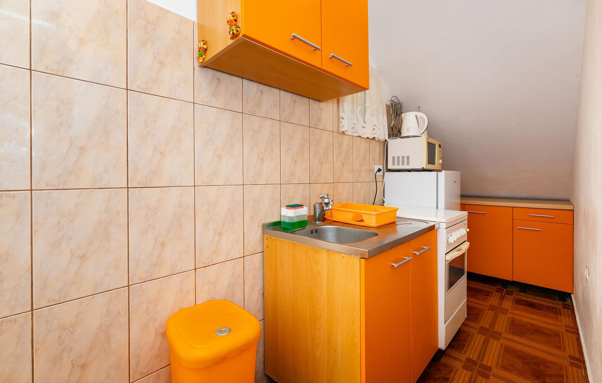 A compact kitchen with orange cabinets, a sink, a microwave, and a stove.