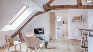 A modern loft with exposed wooden beams, a glass dining table, and a TV in the living area.